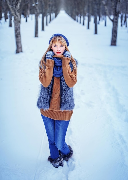 Urocza zimowa dziewczyna ubrana w futrzane dżinsy i sweter bawi się w pięknym zimowym parku