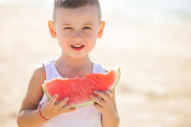 Urocze Dziecko Na Brzegu Morza, Jedzenie Soczystego Arbuza. Rozochocony Dziecko Na Lato Czasie Na Plaży. ładny Mały Chłopiec Na Zewnątrz