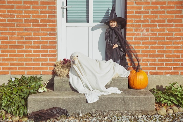 Urocze dziecko z psem na ganku ubrane w kostiumy na halloween.