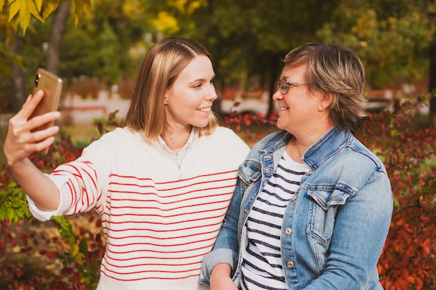 Urocze Kobiety Mama I Córka Siedzą Na ławce W Pięknym Jesiennym Parku I Robią Sobie Selfie Na Telefon