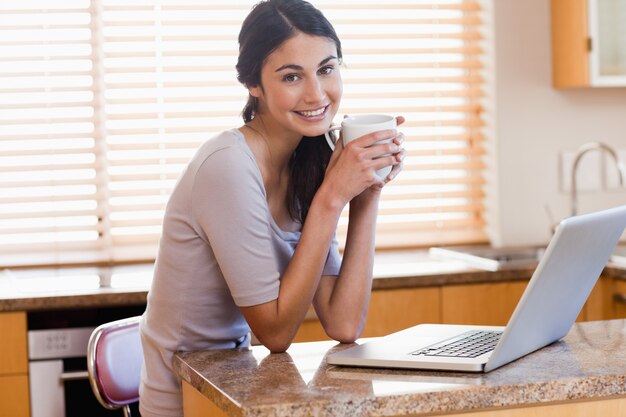 Urocze kobiety za pomocą laptopa podczas picia filiżankę kawy