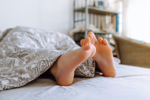 Urocze nogi wystają spod kołdry na łóżku. Widok z boku.