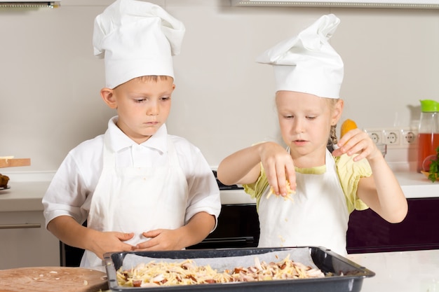 Uroczi mali kucharze poważnie kładą ser na pizzy w kuchni