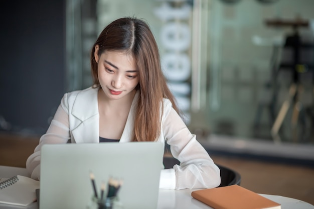 Uroczy bizneswoman azjatyckiego siedzi na laptopie w biurze.