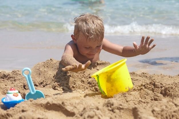 Uroczy chłopiec bawić się na plaży z piaskiem