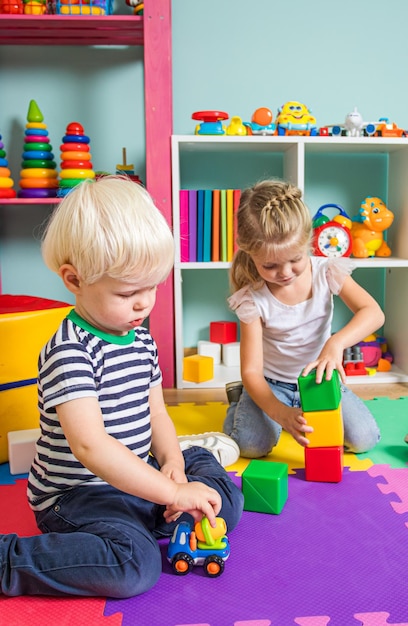 Uroczy chłopiec i dziewczynka bawią się własną zabawką siedząc na podłodze pokrytej kolorowymi matami Rodzeństwo w swoim pokoju z wieloma zabawkami edukacyjnymi