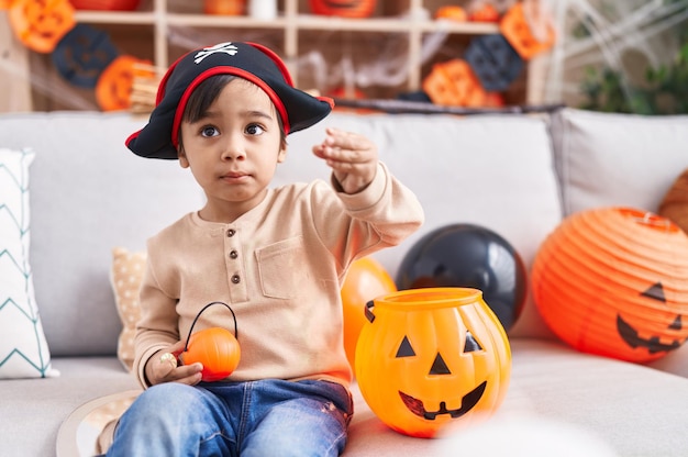 Uroczy latynoski chłopiec mający przyjęcie halloweenowe trzymający kosz dyni w domu