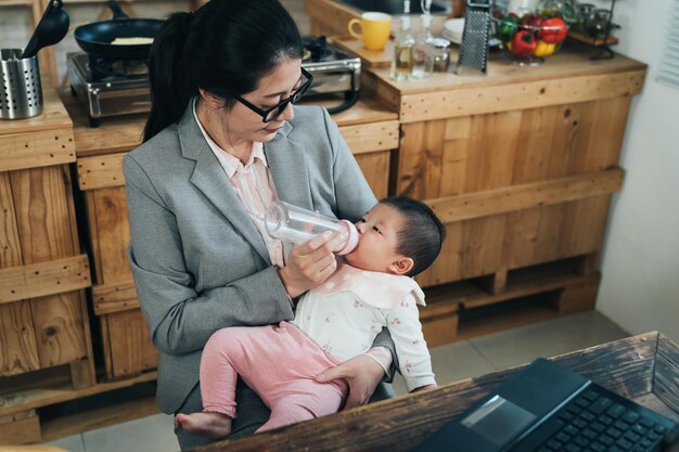 Zdjęcie uroczy maluch leżący wygodnie w ramionach mamy pije z butelki. głodne niewinne dziecko trzymane przez mamę pije mleko w domowym gabinecie.