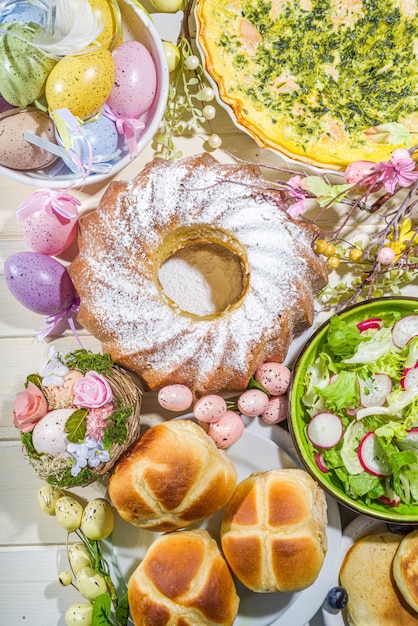 Zdjęcie uroczysta kolacja, brunch wielkanocny. tradycyjne potrawy wielkanocne na rodzinnym stole domowym - pieczone mięso, quiche, wiosenna sałatka, muffinka, kolorowe jajka, gorące bułeczki krzyżowe