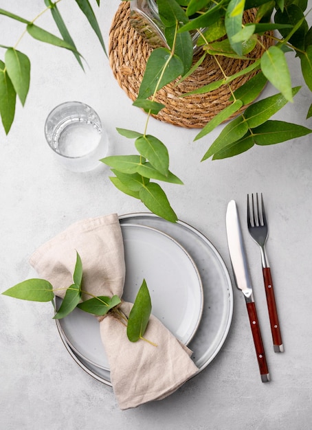 Zdjęcie uroczystościowe ustawienie stołu z dwoma talerzami i szklanką na uroczystość z gałęziami eukaliptusów na jasnym tle koncepcja menu restauracji