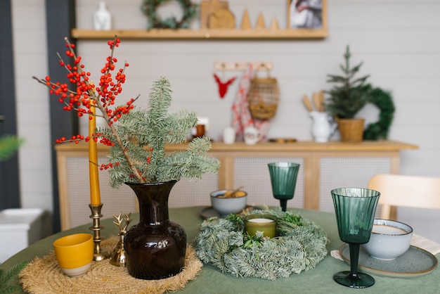 Uroczystościowy stół w kuchni na Boże Narodzenie i Nowy Rok gałęzie świerka w wazonie szkła szkła świeca wieniec na stole