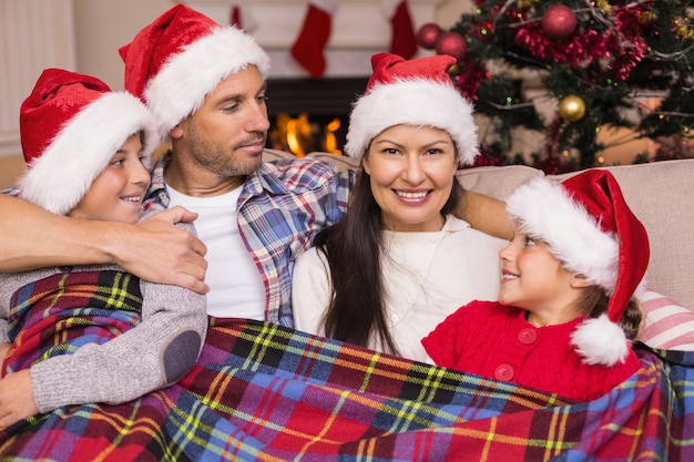 Uroczysty rodziny w santa hat przytulanie pod przykryciem