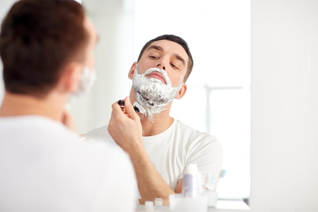 uroda, higiena, golenie, pielęgnacja i koncepcja ludzi - młody człowiek, który chce odzwierciedlić i golić brodę ręczną żyletką w domowej łazience