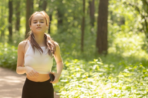 Uroda zdrowie fitness Dziewczyna w słuchawkach biega po parku uśmiechając się