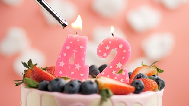 Urodzinowy tort numer 42 różowa świeczka na pięknym torcie z jagodami i zapalniczką z ogniem na tle białych chmur i różowego nieba Widok z bliska