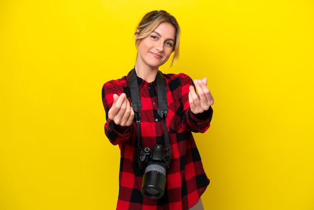 Zdjęcie urugwajska fotograf kobieta odizolowana na żółtym tle robi gest pieniędzy