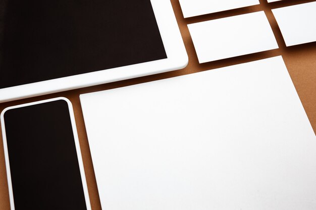 Urządzenie z pustym ekranem unoszącym się nad brązowym tłem. Telefon, tablet i karty. Nowoczesna makieta na reklamę w stylu biurowym. Puste białe miejsce dla koncepcji projektowania, biznesu i finansów.
