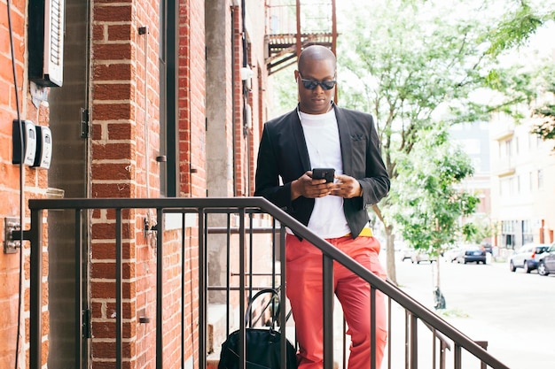 USA, Nowy Jork, Brooklyn, Mężczyzna czeka na schodach, używając smartfona