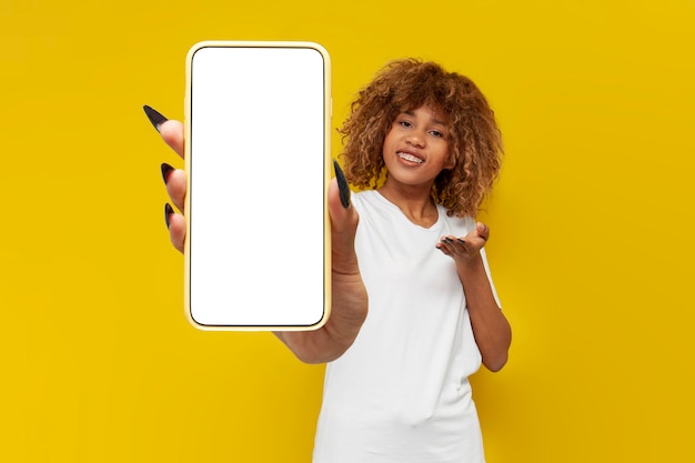 usatysfakcjonowana kręcona Amerykanka z szelkami w białej koszulce pokazuje pusty ekran smartfona