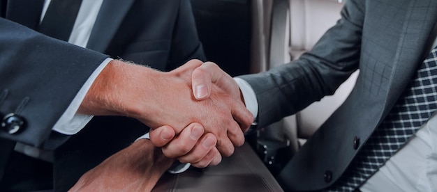 Zdjęcie uścisk dłoni partnerów biznesowych siedzących w prestiżowych samochodach