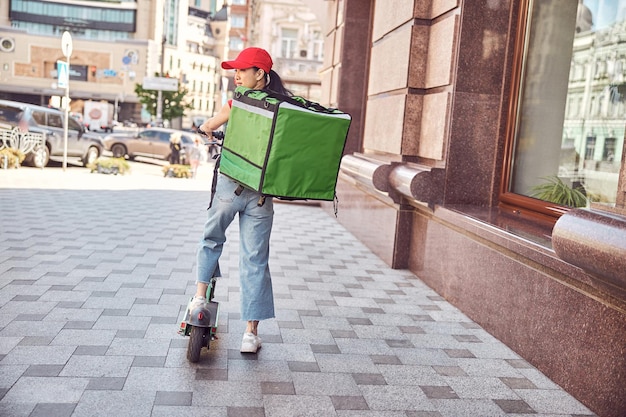 Zdjęcie usługa dostawy kobieta jedzie skuterem w dużym nowoczesnym mieście