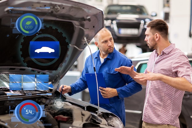 Zdjęcie usługa samochodowa, naprawa, konserwacja i koncepcja ludzi - mechanik z tabliczką i człowiek lub właściciel rozmawiający w warsztacie samochodowym