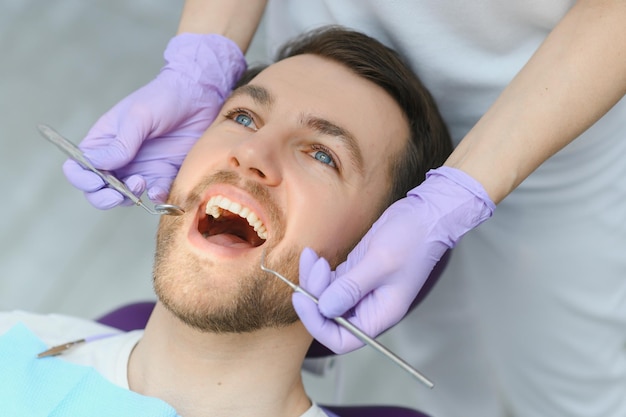 Usługi periodontologiczne Zbliżenie strzał uśmiechający się mężczyzna leczenie w klinice stomatologicznej Lekarz dentysta w rękawiczkach za pomocą sterylnych narzędzi dentystycznych do badania zębów pacjenta płci męskiej