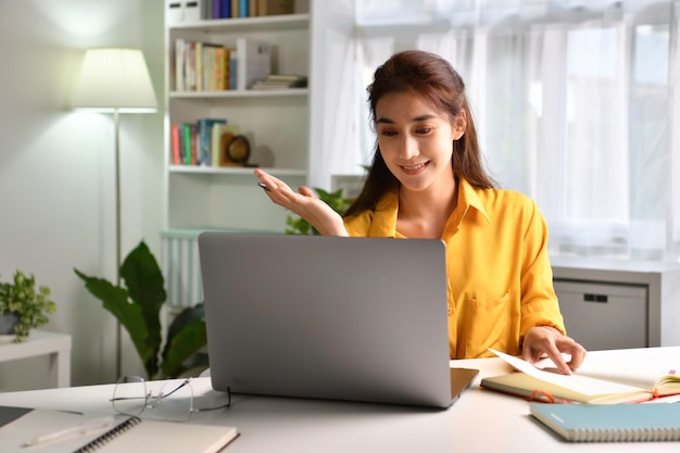 Uśmiech i pozytywne samopoczucie. szczęśliwa młoda azjatycka kobieta freelancer pracuje na komputerze w domu. Atrakcyjna bizneswoman ucząca się online, korzystająca z oprogramowania laptopa, informacji o surfowaniu po sieci lub robiąca zakupy w in