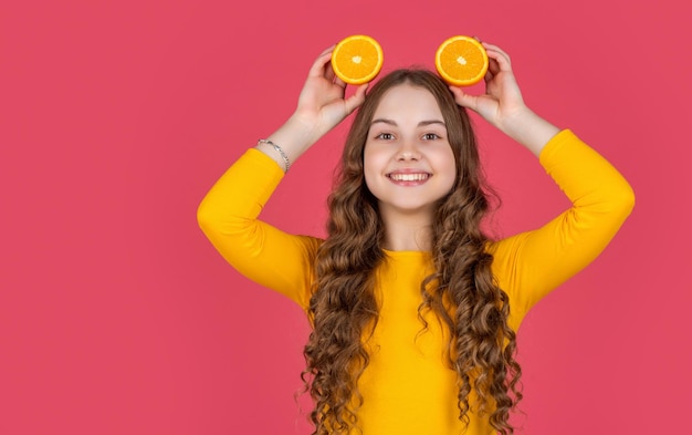 Uśmiech nastolatki trzyma pomarańczowy owoc na różowym tle
