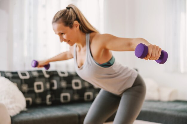 Uśmiechający się mięśni sportsmenka podnoszenia hantli i robienia ćwiczeń fitness w domu.