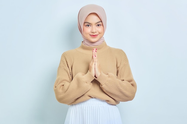 Uśmiechający się piękna azjatycka muzułmańska kobieta w brązowym swetrze, wskazując eid mubarak pozdrowienie na białym tle nad białym tle koncepcja życia religijnego ludzi