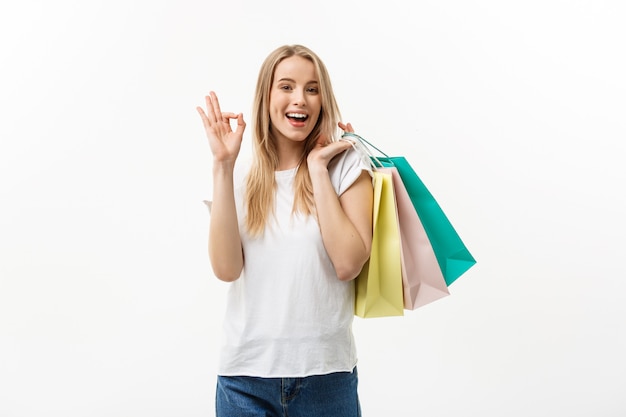 Uśmiechnięci atrakcyjni kobiety mienia torba na zakupy robi ok znakowi na bielu