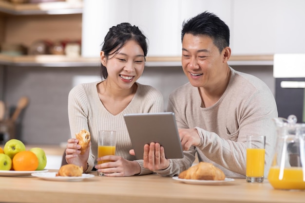 Uśmiechnięci chińscy małżonkowie jedzą śniadanie i używają tabletu