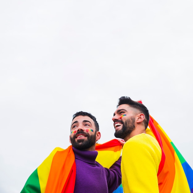 Zdjęcie uśmiechnięci geje z tęczową flagą patrząc w tym samym kierunku