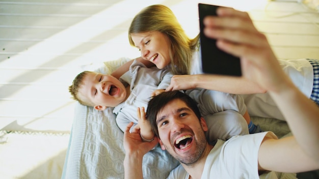 Uśmiechnięci rodzice z dzieckiem robiący selfie rodzinne zdjęcie na łóżku w domu