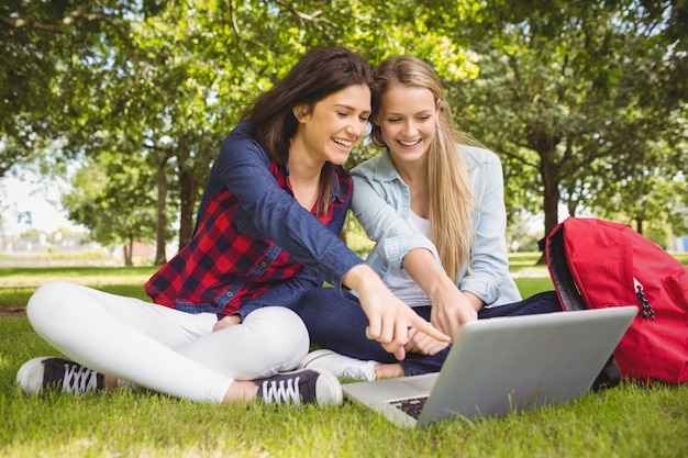 Uśmiechnięci ucznie używa laptop przy parkiem