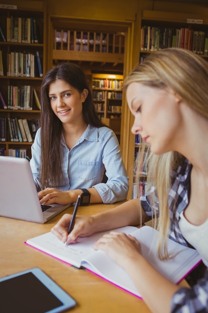 Uśmiechnięci ucznie używa laptop w bibliotece