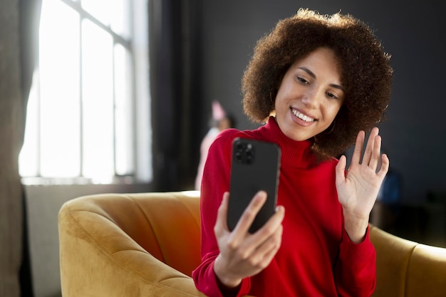 Uśmiechnięta Afroamerykanka trzymająca telefon komórkowy macha ręką podczas rozmowy wideo