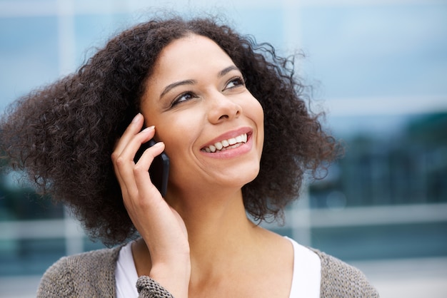 Uśmiechnięta amerykanin afrykańskiego pochodzenia kobieta opowiada na telefonie komórkowym