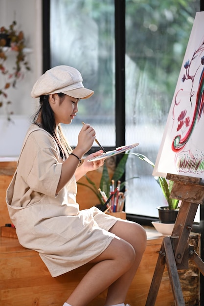 Uśmiechnięta azjatycka dziewczyna malująca na płótnie w warsztacie artystycznym