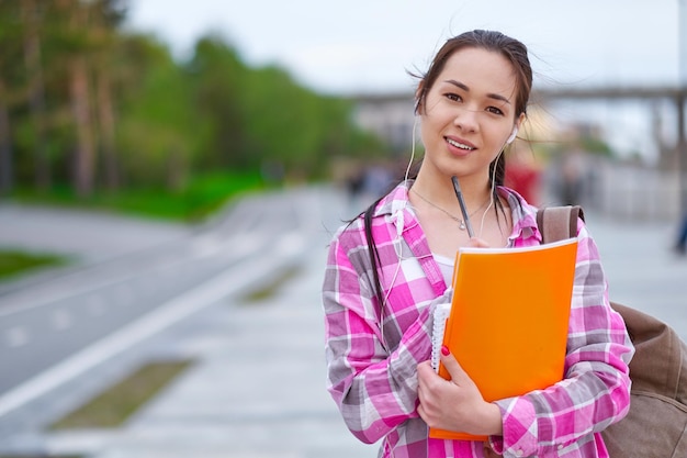 Uśmiechnięta azjatycka studentka z folderami i plecakiem w kampusie edukacyjnym w zielonym parku letnim i koncepcja nastolatka