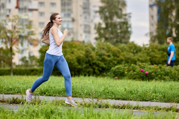Uśmiechnięta biegaczka trenuje w parku dzielnicy mieszkalnej w letni poranek