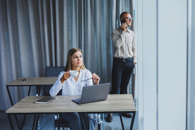 Uśmiechnięta biznesowa kobieta siedzi przy stole z laptopem, trzymając ją plecami do swojego partnera siedzącego przy biurku Koncepcja udanej pracy zespołowej