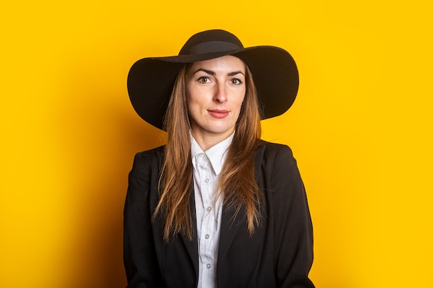Uśmiechnięta biznesowa młoda kobieta w kapeluszu i kurtce na żółto.