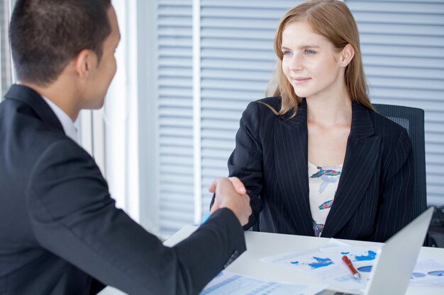 Zdjęcie uśmiechnięta bizneswoman i biznesmen uściskający ręce na stole w biurze