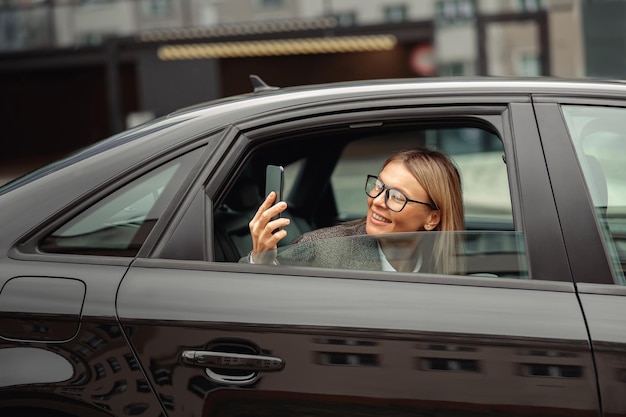 Uśmiechnięta bizneswoman robiąca zdjęcia atrakcji z tylnego siedzenia samochodu w drodze do pracy