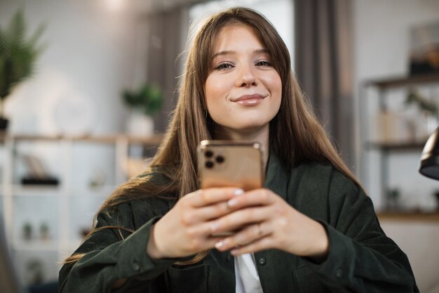 Uśmiechnięta bizneswoman używająca nowoczesnego smartfona do czatu wideo w pracy