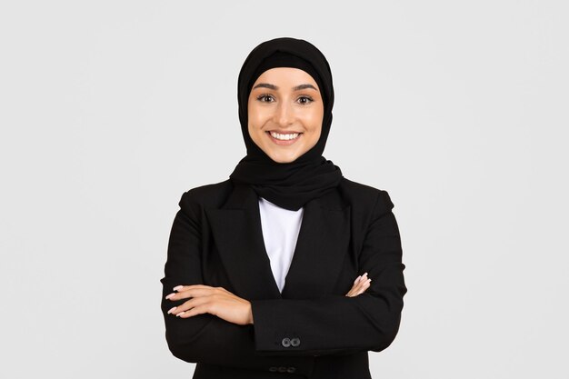 Uśmiechnięta bizneswoman w hidżabie i formalnym ubraniu z skrzyżowanymi ramionami