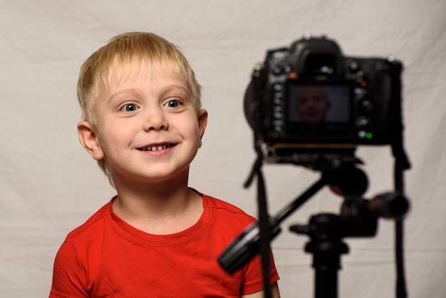 Uśmiechnięta blond chłopiec przed kamera obiektywem. Mały bloger wideo. Domowe studio