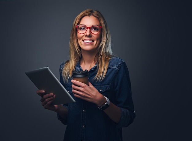 Uśmiechnięta blond kobieta w okularach posiada tablet Pc i zabrać filiżankę kawy.